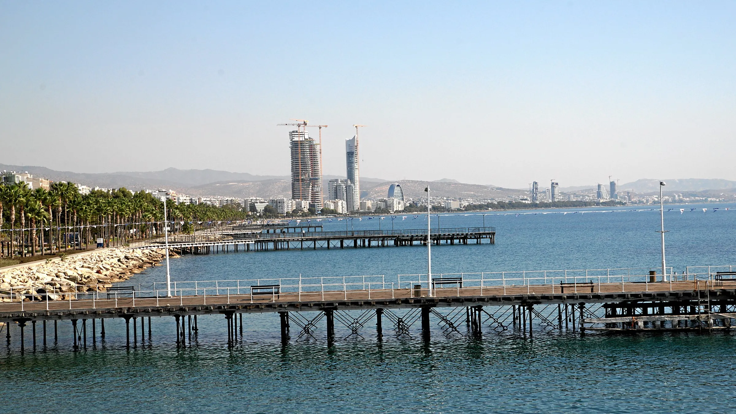 Holzstege an der Strandpromenade von Limassol mit der Skyline im Hintergrund.