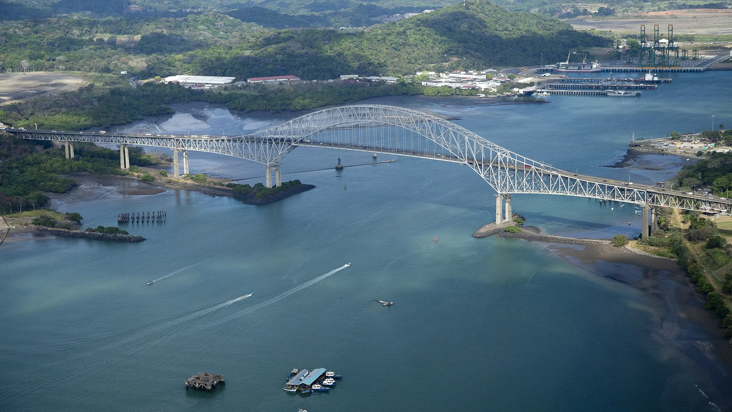 Luftaufnahme der Puente de las Américas über die Kanaleinfahrt, mit grünen Hügeln auf der Westseite.